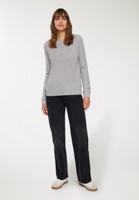 Szary sweter z dzianiny z prążkowanym dołem i mankietami, sparowany z luźnymi czarnymi dżinsami i białymi trampkami. Stylizacja ma swobodny, luźny krój.