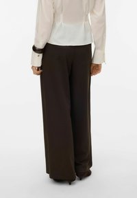 Hvid bluse med en figursyet ryg og manchetknapper, kombineret med brede, brune bukser, der fremhæver en glat tekstur og skræddersyet pasform.