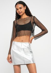 Čierny sieťovaný crop top s dlhým rukávom na čiernom priliehavom tielku, doplnený o lesklú striebornú mini sukňu s hladkou textúrou a čistými švami.