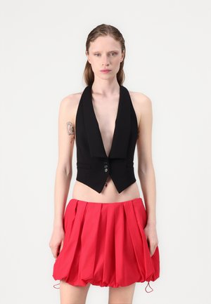 Zwarte mouwloze vest met een diepe halslijn en een enkele knoopsluiting, gecombineerd met een rode, volumineuze, geraffineerde minirok.