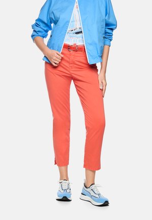 Blue jacket over white nautical graphic tee, coral pants with matching belt, and blue and white sneakers on a standing person.