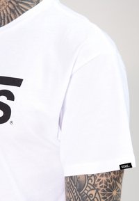 Biała bawełniana koszulka z dużym czarnym logo z przodu. Krótkie rękawy i mała metka marki na lewym rękawie.