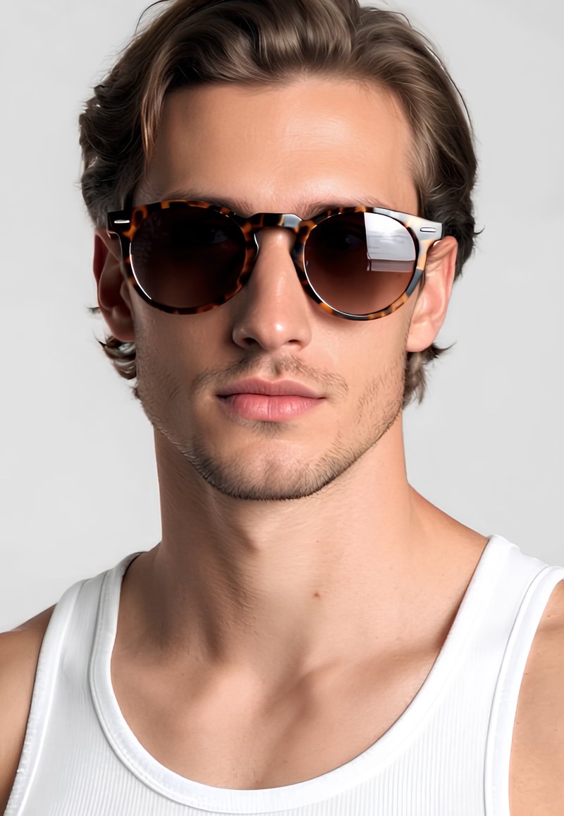 Occhiali da sole tondi in tartaruga con lenti scure e dettagli argentati sui lati, indossati da un modello in canottiera bianca.