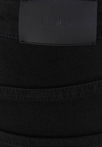 Sombrero tipo bucket de mezclilla negra con tela texturizada. Presenta un parche de cuero negro liso con el logotipo "Bershka" en relieve. La costura es visible a lo largo de los bordes.