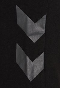 Dos flechas grises apuntando hacia abajo sobre un fondo de tejido de punto negro, mostrando textura y ligeras arrugas.