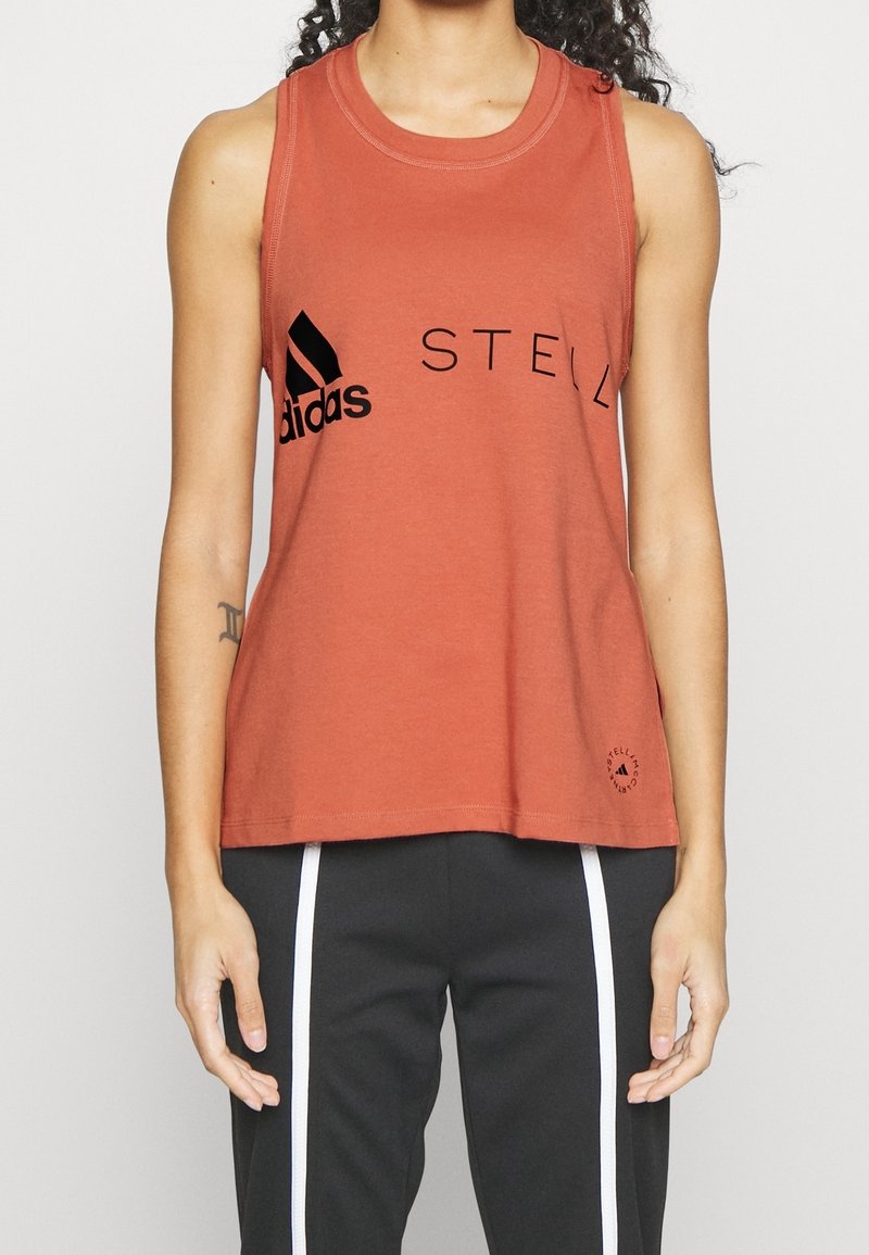 Rostfärgad ärmlös tanktopp i bomull, med en svart Adidas-logga och texten "STELL". Rundad halsringning och lös passform.