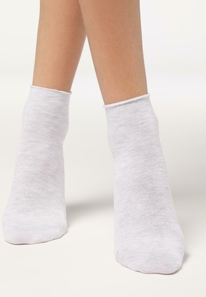 Calcetines tipo anklet en un color gris claro, hechos de una tela suave y elástica. Tienen un diseño sencillo con un borde acanalado en la parte superior y una puntera sin costuras.