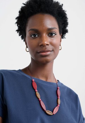 Necklace with red and brown leaf-shaped beads on a string, worn over a navy blue top with a round neckline and short sleeves.