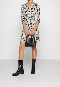 Svart och vit klänning med omslagdesign, 3/4 lång ärm och kedjemönster. Kombination med svarta ankelstövlar och en liten svart handväska.