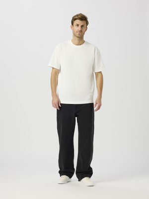 Camiseta blanca de manga corta, corte relajado, combinada con vaqueros negros de pierna ancha. La modelo lleva zapatillas blancas. Diseño sencillo, tejido ligero.