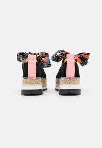 Chaussures en daim noir avec des nœuds en tissu coloré à motifs, semelles espadrille tissées de couleur caramel et semelles intermédiaires blanches. Présentent des accents roses au talon.