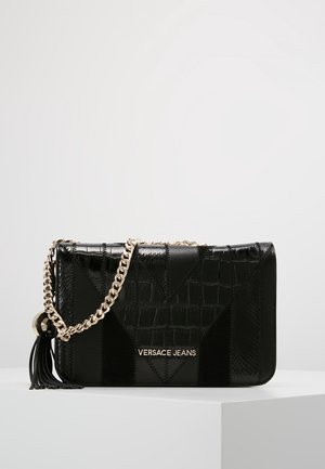 Sac à épaule noir Versace Jeans avec une texture patchwork brillante, bandoulière chaîne dorée, détail pompon et logo doré sur le devant.