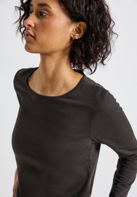 Haut noir à manches longues avec un col rond, texture douce et forme ajustée, mettant en valeur un tissu lisse et des détails de design minimalistes.