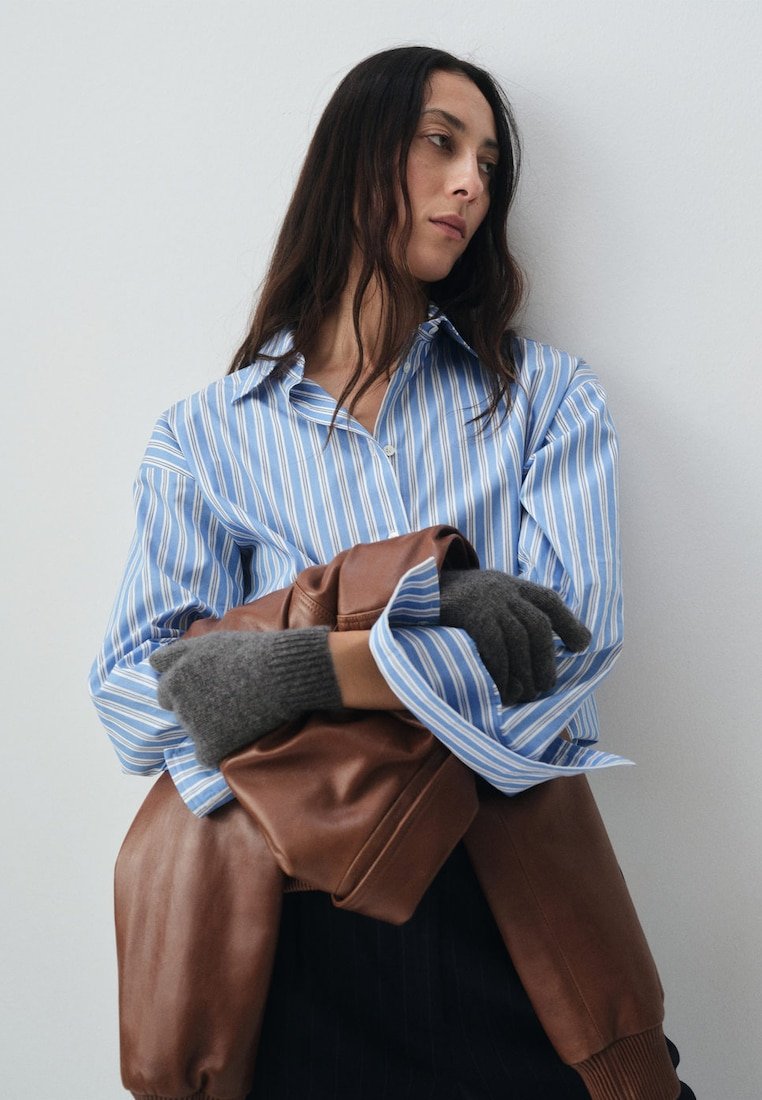 Blue and white striped shirt with buttoned collar, gray gloves, and a brown leather jacket draped over the arm, against a neutral background.