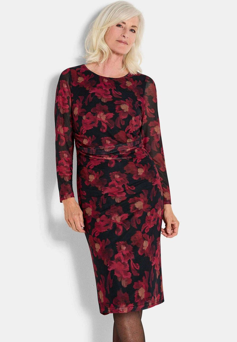 Schwarzes Kleid mit langen Ärmeln und floralem Muster in Rot und Beige. Enganliegende Silhouette, weicher Stoff, knielang mit runder Ausschnitt.