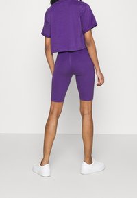 Růžový zkrácený tričko a odpovídající cyklistické šortky, vyrobené z měkkého materiálu. Nosené s bílými teniskami, ukazujícími přiléhavý design.