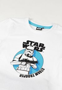 Camiseta de algodón blanca con un gráfico de Stormtrooper en negro y azul, con el texto "STAR WARS" encima del personaje y un fondo circular azul.