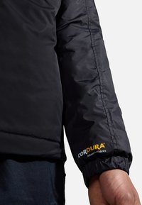 Black insulated jacket sleeve made of CORDURA fabric. Features elastic cuff, visible stitching, and logo detail in yellow. Soft texture.