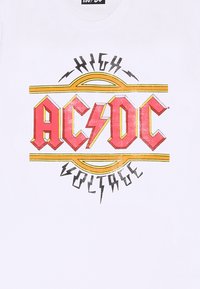 Biała koszulka z czerwoną i żółtą grafiką AC/DC "High Voltage" z akcentami błyskawic i wyrazistym tekstem w stylizowanej czcionce.