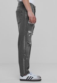Jeans gris desgastados con detalles rasgados, corte recto y un lavado desvaído. Combinados con zapatillas blancas y grises con rayas negras.
