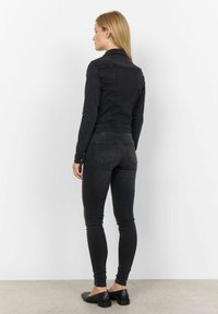 Svart denimjacka med långa ärmar, figursydd design och accentstitching på ryggen, i kombination med svarta skinnyjeans och platta skor.