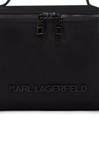 Fekete nylon táska kettős cipzárral, a "KARL LAGERFELD" felirattal domborítva. Simább textúra, téglalap alak, minimalista dizájn.