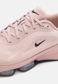 Ljusrosa träningsskor med nätövre, svart Nike-logotyp och synlig luftdämpning i sulan. Har snörning och strukturerad tyg.