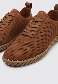Baskets en suede perforé marron avec lacets plats, dotées d'une semelle texturée et de coutures contrastées, conçues pour la respirabilité et le confort.
