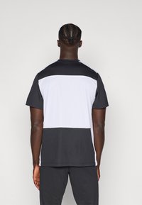 Koszulka sportowa z krótkim rękawem, charakteryzująca się designem w kolorze czarno-białym, z teksturowanym materiałem i okrągłym dekoltem.