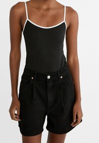 Body negro sin mangas con ribete blanco, combinado con pantalones cortos de mezclilla negros de talle alto que cuentan con bolsillos frontales y detalles en hardware de cobre.