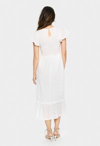 White dress with a fitted bodice, flared sleeves, and a lace-like texture, featuring a keyhole back and a ruffled hem.