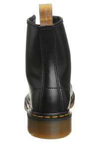 Černé kožené kotníkové boty s hladkým povrchem, žlutým prošíváním, texturovanou gumovou podrážkou a poutkem s nápisem "Dr. Martens."