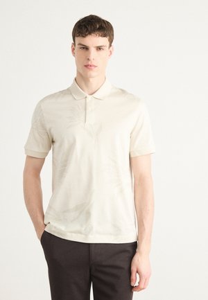 Camisa polo de manga corta en beige claro con un sutil patrón floral, con un collar clásico y tapeta de tres botones, hecha de un tejido suave.