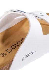 Sandalía blanca de cuero con plantilla de corcho, con un detalle de hebilla metálica y una suela texturizada. Nombre de la marca "palado" visible en la plantilla.