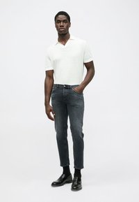 Polo de manga corta gris claro, jeans ajustados gris oscuro, y mocasines negros. Tejido suave y corte a medida.