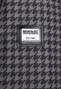 Tissu pied-de-poule noir et gris avec une étiquette rectangulaire cousue indiquant "Regatta Great Outdoors, Est. 1981, For Every Adventure."