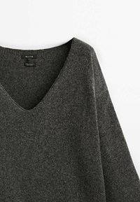 Mørkegrå sweater med V-hals og lange ærmer, lavet af en blød, tekstureret uldblanding. Har et enkelt, rent design med få detaljer.