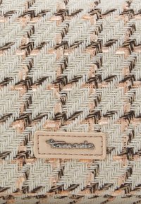 Tissu tissé beige et marron avec un motif en chevrons et une étiquette rectangulaire cousue avec un logo en métal « Tamaris ».