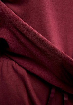 Vīna sarkana auduma ar maigu faktūru; drapēts dizains ar vieglu mirdzumu un savākts pie jostasvietas, papildināts ar saskaņotām lentītēm.