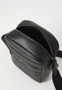 Black crossbody bag featuring a combination of smooth leather and textured fabric, with dual zippers and an adjustable strap.