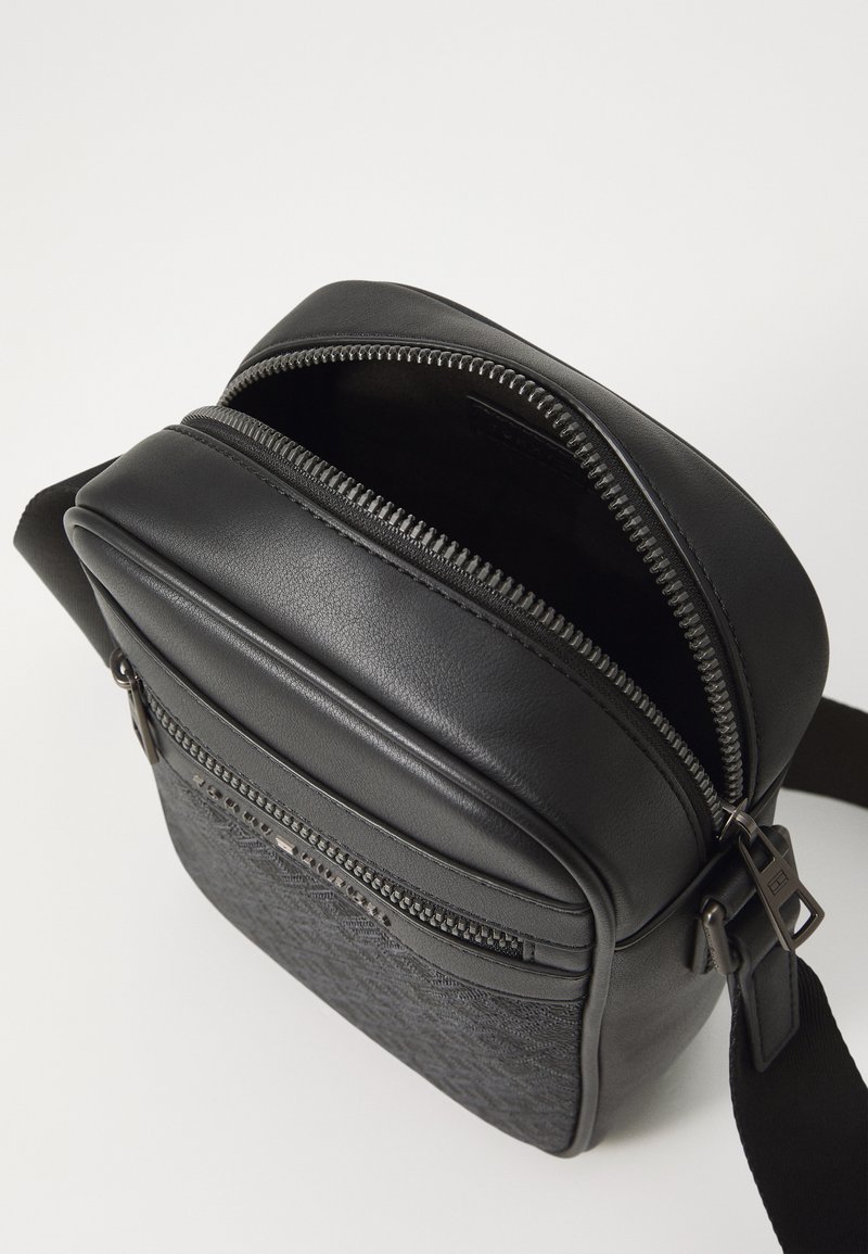Bolso bandolera negro que presenta una combinación de cuero suave y tela texturizada, con cremalleras dobles y una correa ajustable.