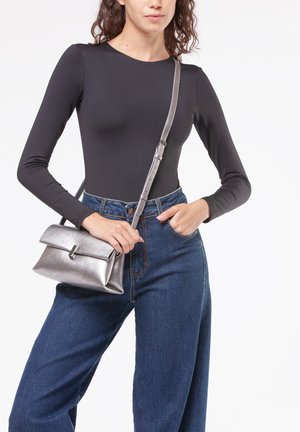 Borsa metallica argento con pattina pieghevole e dettaglio con chiusura, abbinata a un top aderente nero a maniche lunghe e jeans blu a gamba larga.