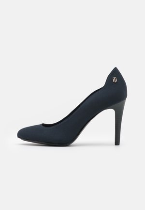 Marineblaue Pumps mit spitzem Zeh und schlankem Absatz sowie kleinem metallischem Logo an der oberen Ferse.