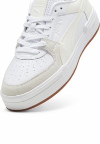 Vit sneaker med en kombination av slätt läder och mocka, perforerad tå, vita snören och en sula av gummimaterial; har diskret varumärkesdetaljering.