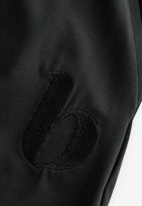 Zwarte stof met een gladde textuur en een grote zwarte geborduurde letter 'b' op het oppervlak. Eenvoudig en ongecompliceerd ontwerp.