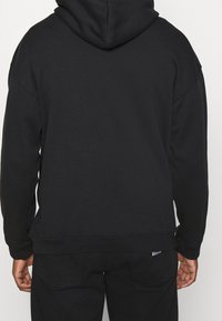 Black cotton hoodie with a spacious fit, kangaroo pocket, and ribbed cuffs. Features a drawstring hood and minimal branding on the hem.