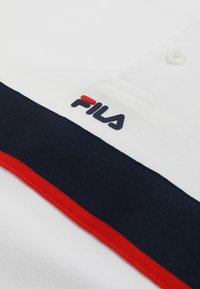 Polo blanc avec des rayures horizontales bleu marine et rouges et un logo FILA cousu près des boutons.