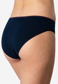 Boxers en coton bleu marine avec une texture lisse, présentant des coutures contrastantes rouges le long de la ceinture et des ouvertures de jambe.