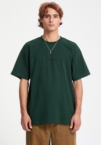 Ciemnozielona bawełniana koszulka z krótkim rękawem, luźny krój, wyhaftowane logo "VOLCOM" na czarno. Prosty i klasyczny design.