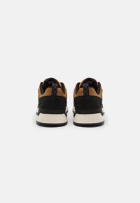 Baskets marron et noires avec dessus en daim et mesh, forme arrondie, et semelle blanche épaisse avec des accents noirs.